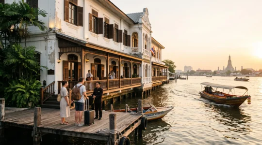 A colonial-era riverside hotel in a converted historic building beside the Chao Phraya river, with guests arriving on a wooden pier at golden hour.