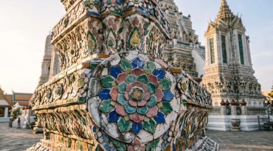 Close view of a Thai temple spire covered in intricately arranged broken porcelain shard mosaics photographed in early morning light.